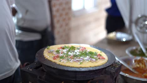 primer plano de un hombre preparando dosa, agregando verduras como cebolla encima con aceite de cocina en una tienda
