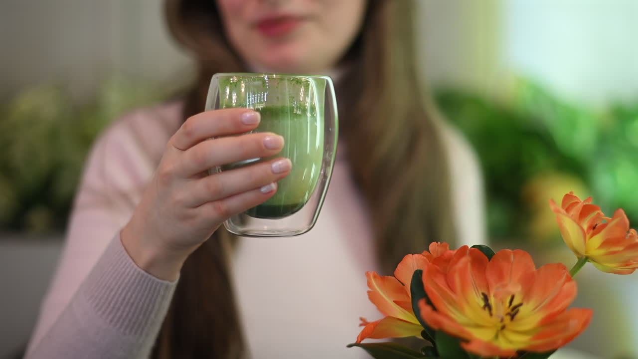 Woman in eco friendly restaurant drinking matcha. Flowers in foreground
