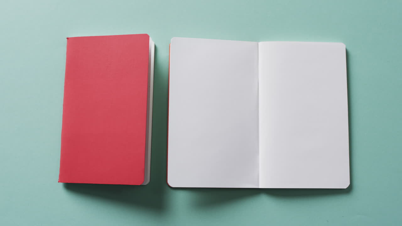Close up of open blank book and closed red book with copy space on green background in slow motion