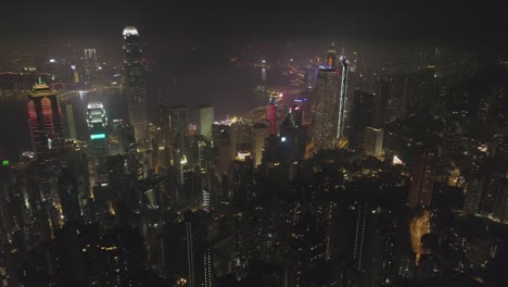 illuminated hong kong skyline and victoria harbour at night. aerial view. drone is flying forward, camera is tilting up. establishing shot. 60 fps.