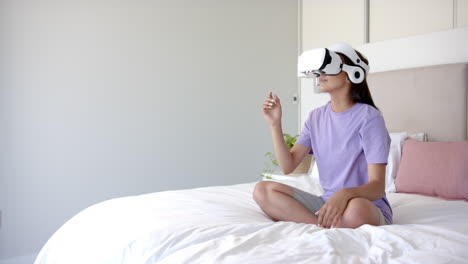 using vr headset, woman sitting cross-legged on bed, interacting with virtual world, copy space