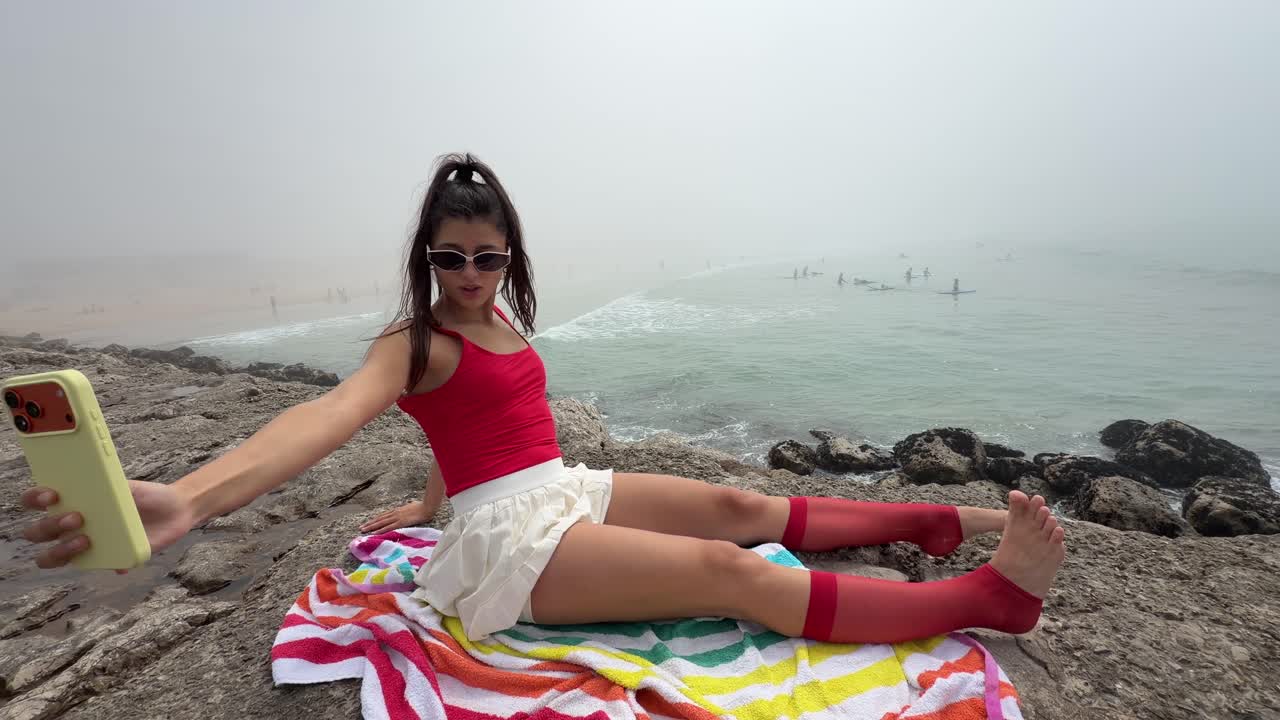 Giovane donna in posa per un selfie su una spiaggia rocciosa in una giornata nebbiosa
