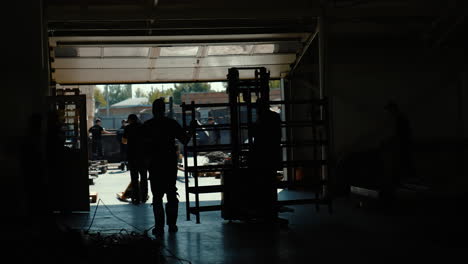 vinnytsia, ukraine - january 19, 2023: dark silhouettes of people, workers with cargo moving to exit to gate of warehouse