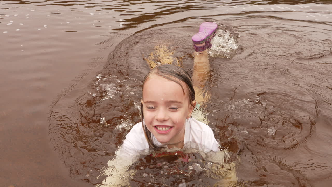 진흙 투성이의 강에서 수영하고 튀는 즐거운 어린 소녀, 슬로우 모션