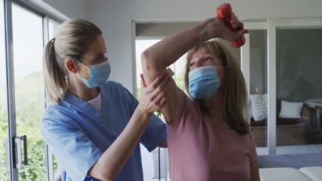 female health worker assisting senior woman to exercise with dumbbells at home