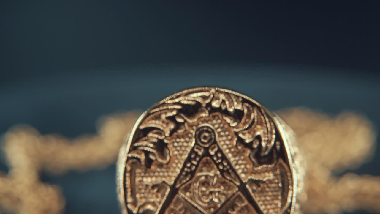 A macro detailed shot of a golden textured freemasons ring, on a mirror reflection stand, illuminati symbol, studio light, 4K video, tilt up movement, necklace shallow depth of field