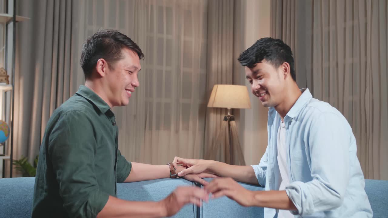 Young Asian Adult Gay Couple Spend Time At Home. Two Happy Men In Love In Casual Clothes Gently Hold Hands. Cute Lgbt Relationship Content