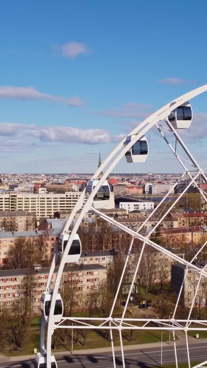 Vertical Ferris wheel spinning above cityscape on a sunny day in Riga, Latvia