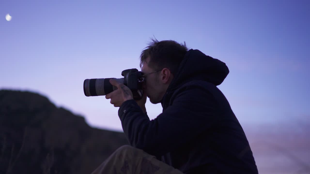 fotógrafo masculino tomando fotografías en la caminata por el pico de la montaña al amanecer