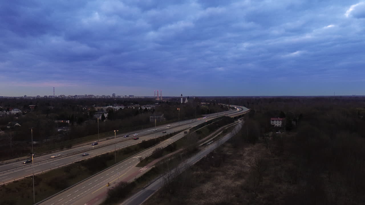 Aerial: Capital City of Warsaw cityscape at sunset with skyscape, road and traffic in Masovian, Poland, crane up drone shot