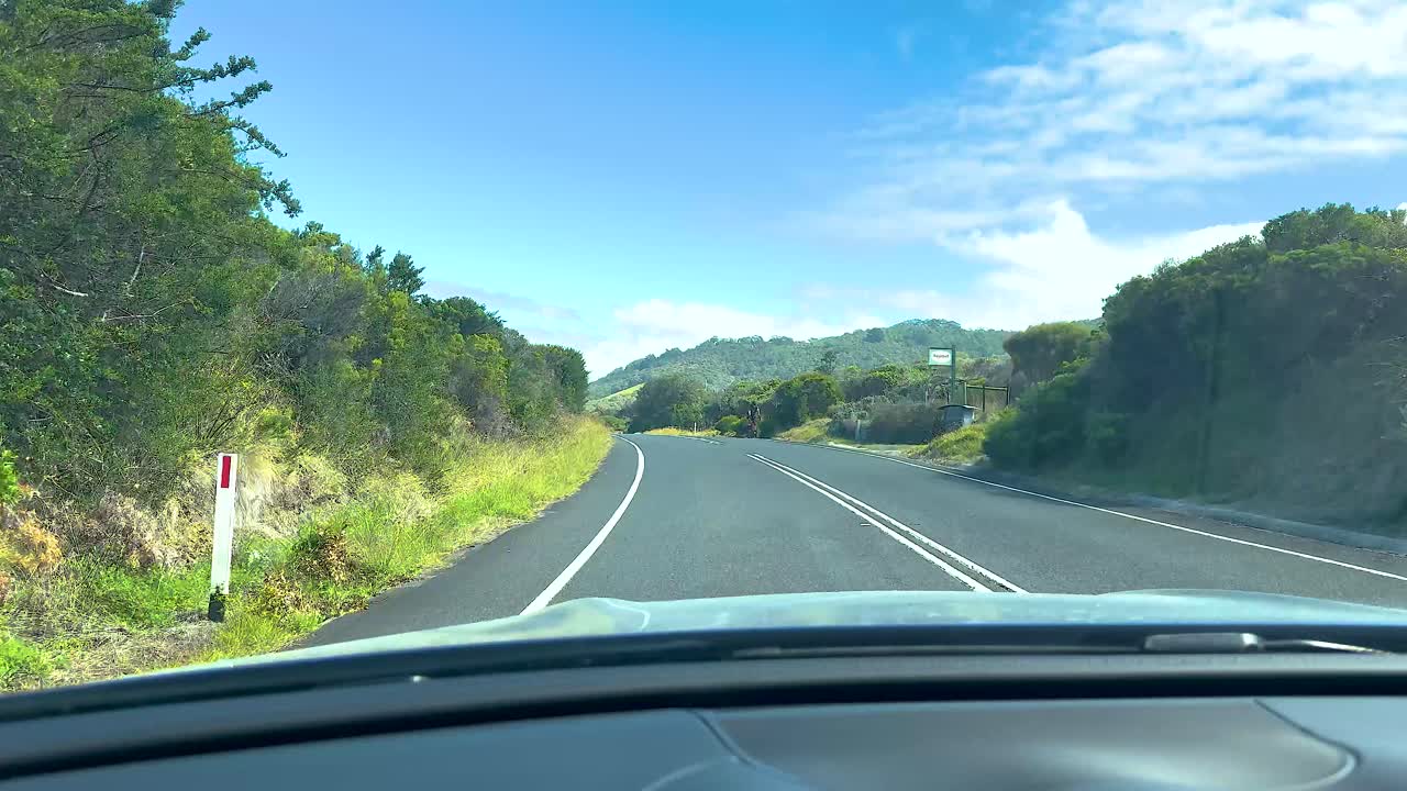 A car journey on a sunny day along the picturesque Great Ocean Road, capturing lush greenery and clear blue skies
