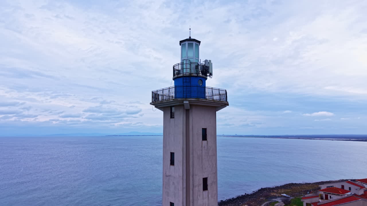 Un faro si erge maestoso contro un cielo nuvoloso vicino all'acqua, fornendo guida a barche e navi.