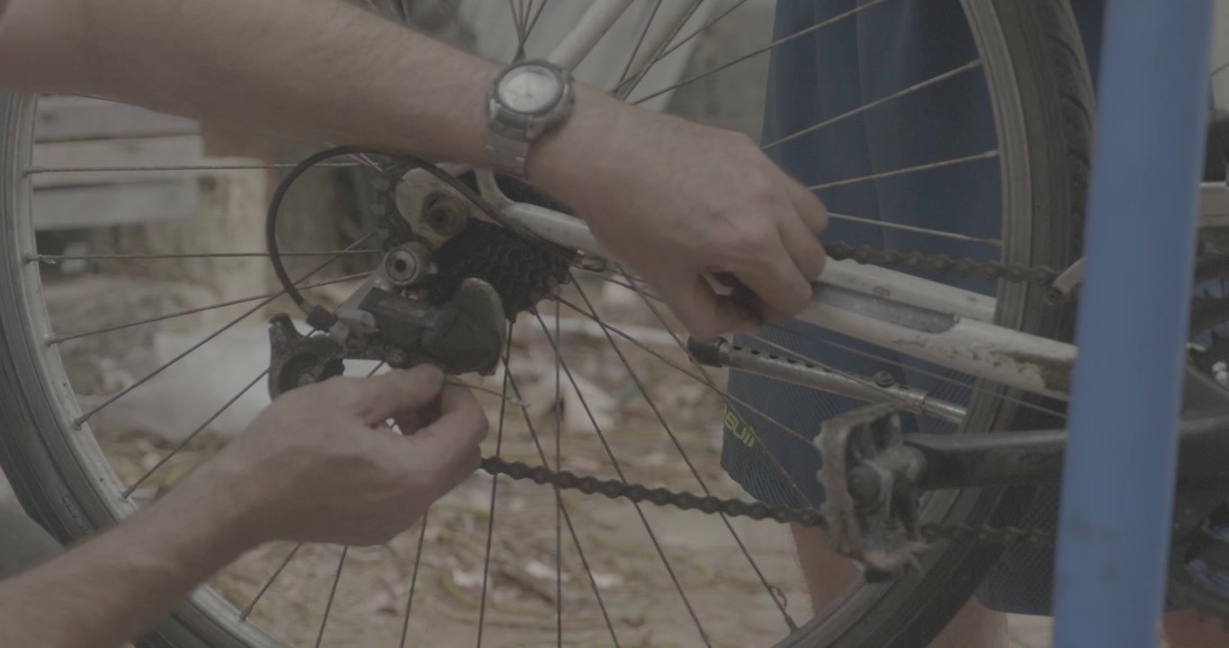 Passando fio de metal na roda traseira. Pai e filho consertam e fazem a manutenção de uma bicicleta de forma artesanal