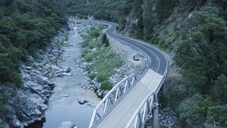 Pequeño-Puente-Cruza-El-Agua-Que-Fluye-Para-Conectar-Dos-Lados-Del-Valle,-Antena