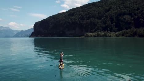 aerial, drone shot of a stand up paddler on a yellow sup, stand up paddle, in the middle of a fjord lake in switzerland while summer