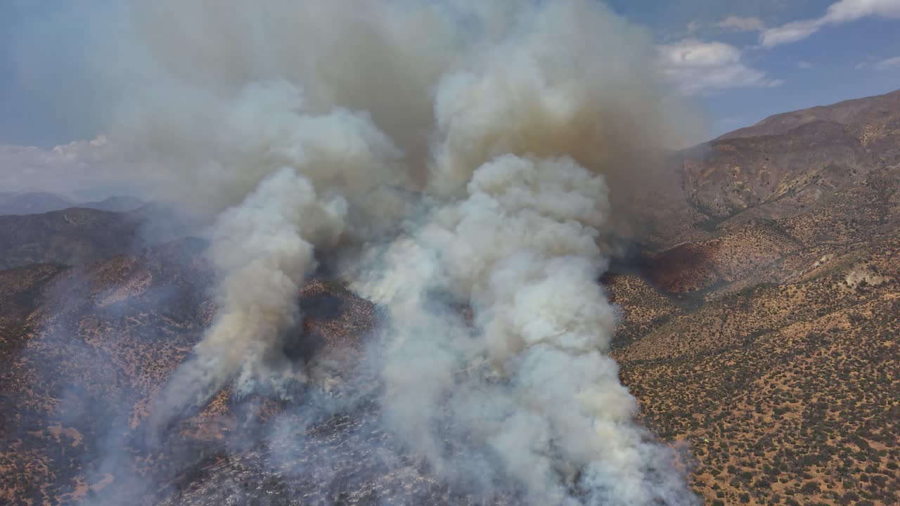 Ripresa aerea con drone di due distinte colonne di fumo bianco di un incendio che si alzano da una cresta montuosa arida in Cile e video 4K