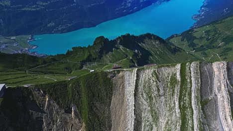vista aérea de una ladera, revelando el pico más alto de una montaña, un lago azul prístino y montañas cubiertas de nieve en la distancia