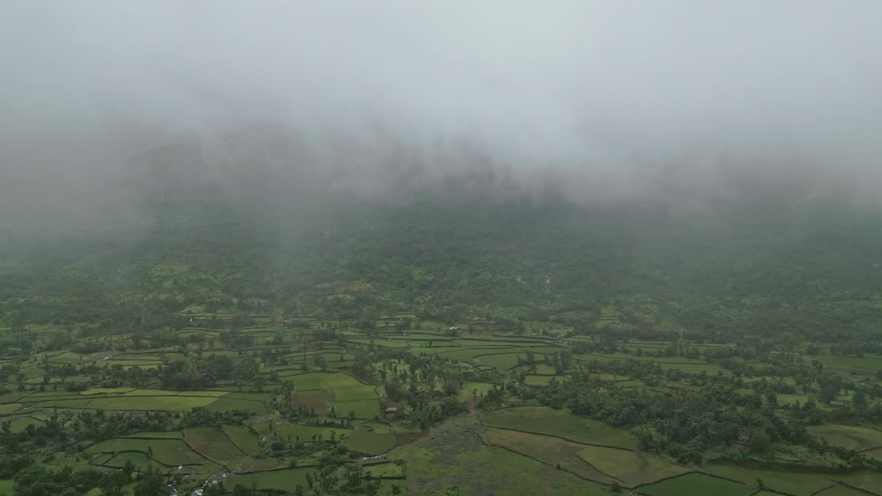 A breathtaking drone view of Bhandardara, Maharashtra, with lush green fields, misty mountains, and monsoon fog weaving through the serene landscape, creating a dreamy, picturesque scene 4K