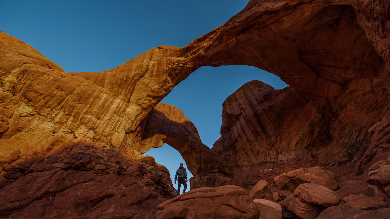 Cinemagraph time-lapse of young man watching golden sunrise at sandstone Double Arch in Arches National Park, Utah, USA