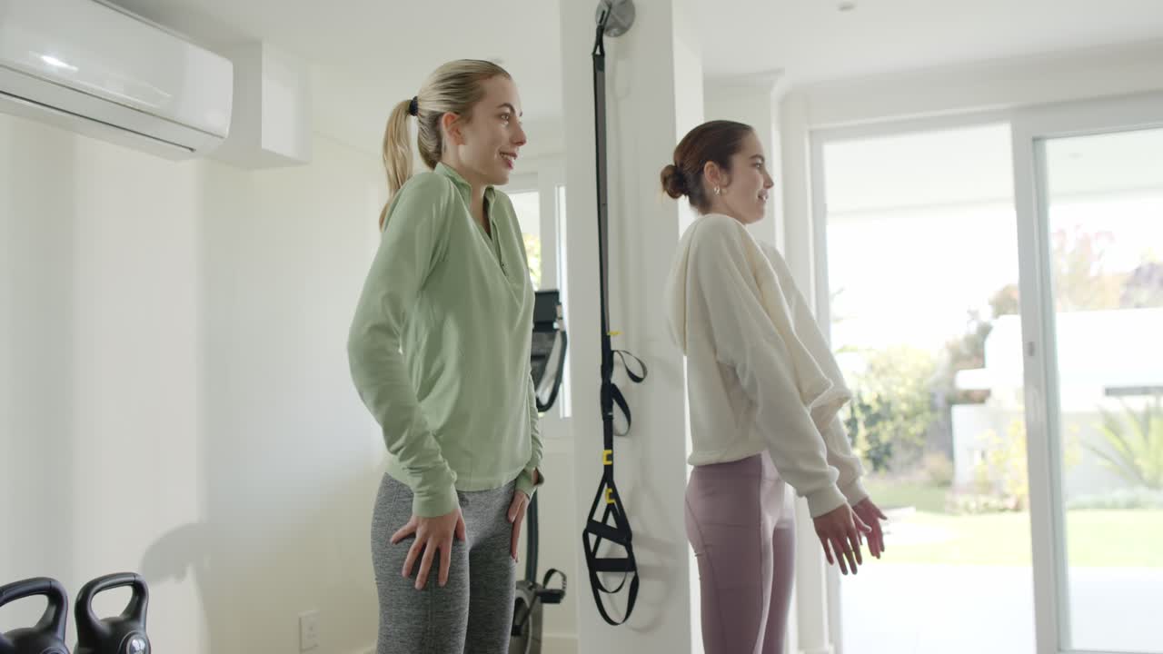 Due donne si spostano sui talloni spingendo in avanti i fianchi per allungare la schiena in palestra con cinghie TRX