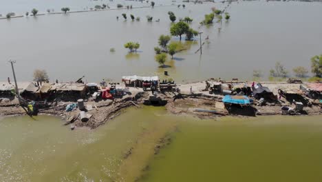 drone view of lone elevated road housing makeshift camps for flood refugees surrounded by expansive flood waters in rural jacobabad, sindh