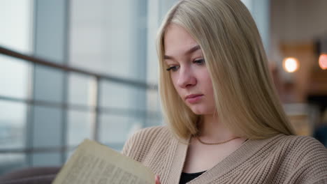 joven sentada pensativa en un ambiente interior acogedor, volviendo una página de su libro mientras se absorbe en la lectura, con una expresión tranquila y enfocada