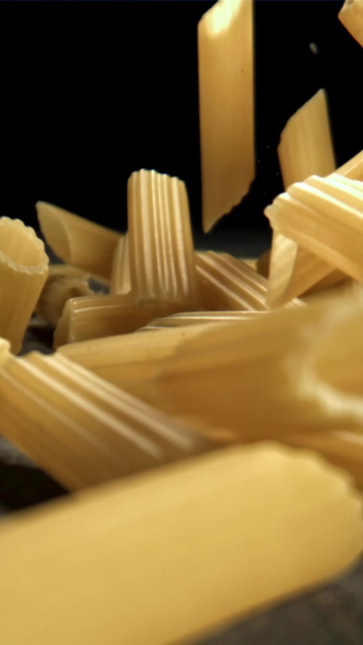 Primo piano di pasta penne secca che cade su una superficie scura