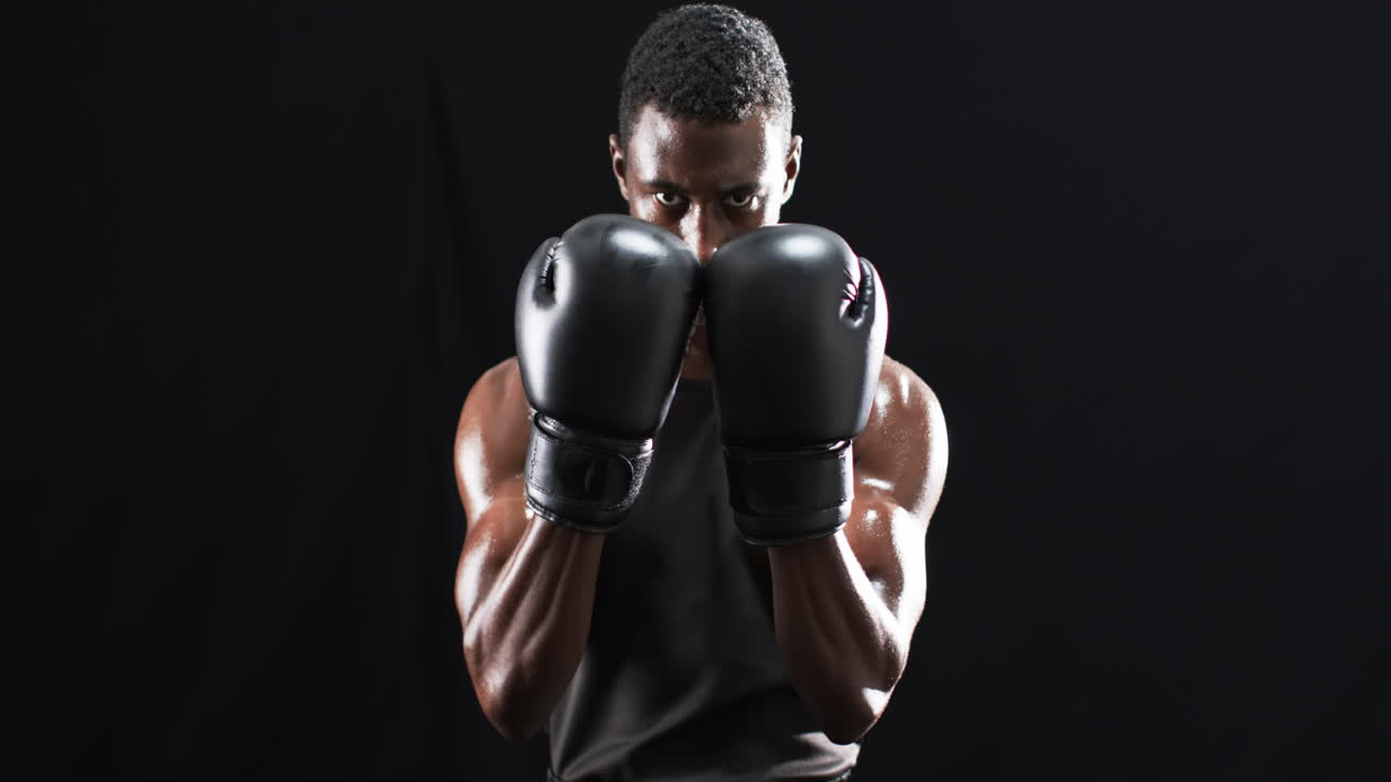 boxeador afroamericano en posición defensiva sobre un fondo negro