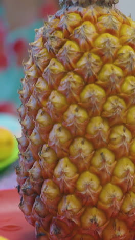 yellow pineapple with bright green top on red plate against blurry lady eating fruits extreme close view
