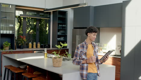 holding tablet and drinking coffee, teenage boy standing in modern kitchen