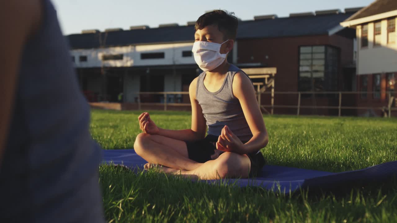 niño con máscara facial realizando yoga en el jardín
