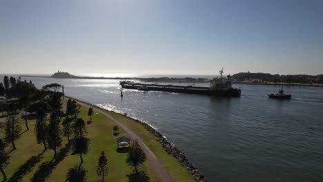 bulker ship and tugboat navigating at mouth of hunter river towards tasman sea in stockton, nsw, australia. wide aerial shot