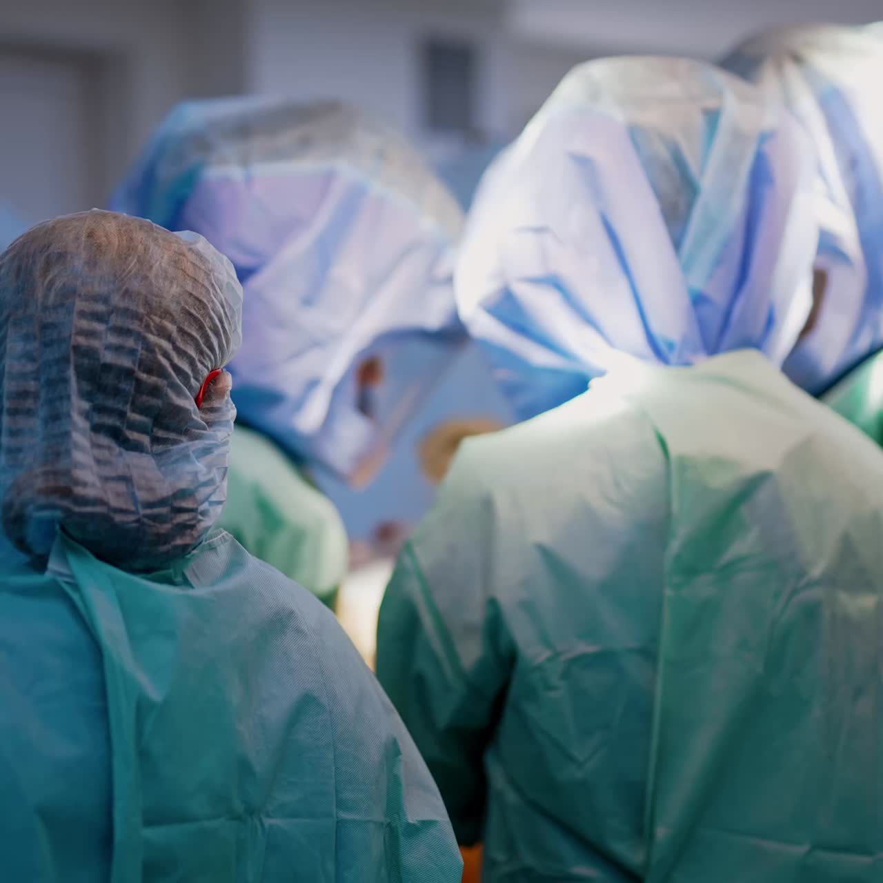 Rear view of a nurse watching the team of doctors work at surgery. Three surgeons stand around the operational table