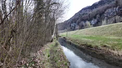 A-sweeping-vista-reveals-a-water-channel-flowing-against-the-backdrop-of-the-Swiss-mountains,-encapsulating-the-concept-of-harmony-between-nature's-elements