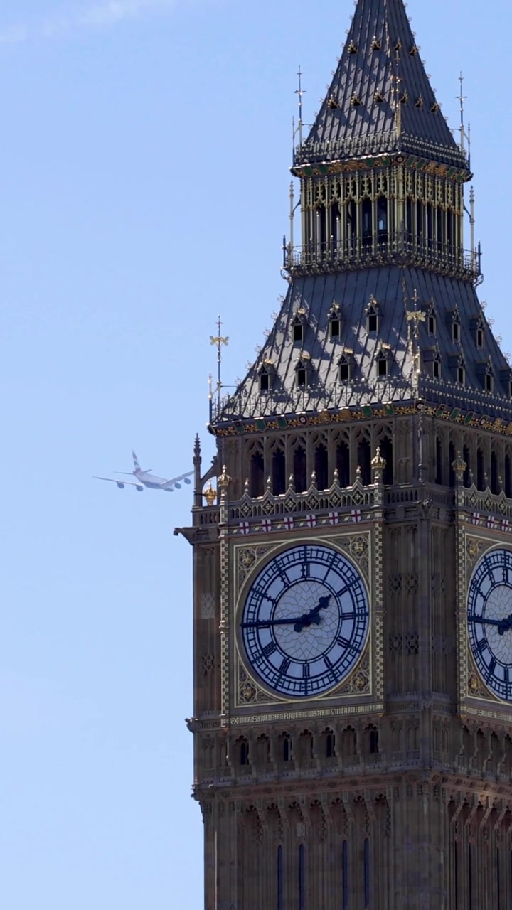 A commercial airplane glides through a clear blue sky past the historic clock tower.