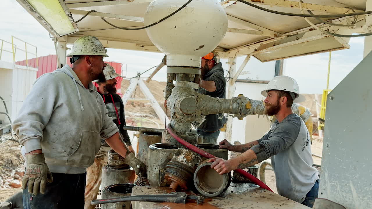 Four bearded men in helmets are standing at the site for drilling gas. Cooperative crew working at natural resources production industry.