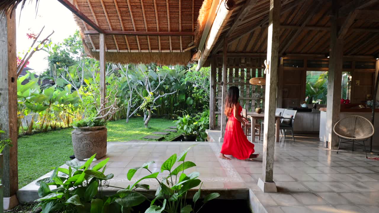 インドネシアのバリ島のオープンコンセプトヴィラを歩く、赤いマキシドレスを着た若いアジア人女性