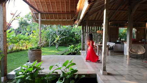 young asian girl in red maxi dress walking through open concept villa in bali indonesia