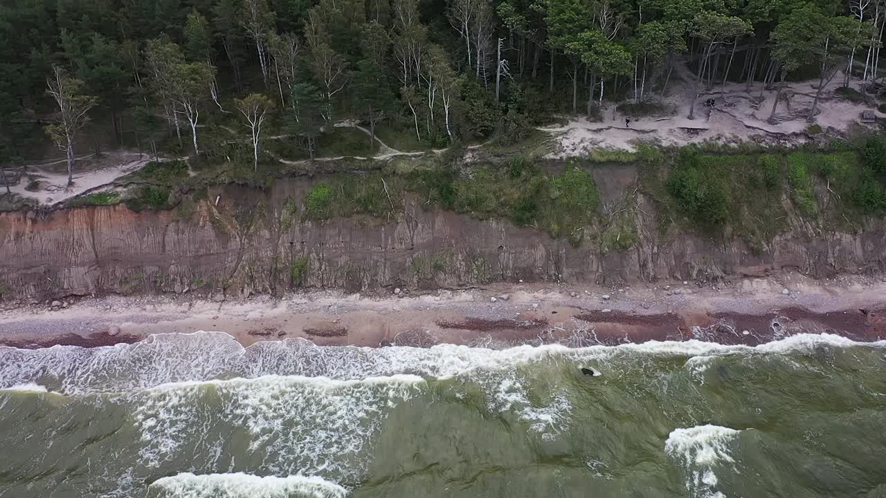 un dron revela la grandeza de una alta costa de acantilado en el mar báltico en lituania, donde las olas imponentes chocan contra las rocas, rodeadas de aguas caprichosas y coloridas