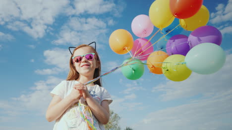 a cheerful girl with balloons is standing on a green meadow enjoy the warmth and fly of the concept