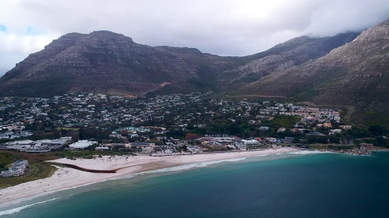 un avión no tripulado captura una impresionante vista aérea de una pequeña ciudad oceánica ubicada al pie de colinas nubladas