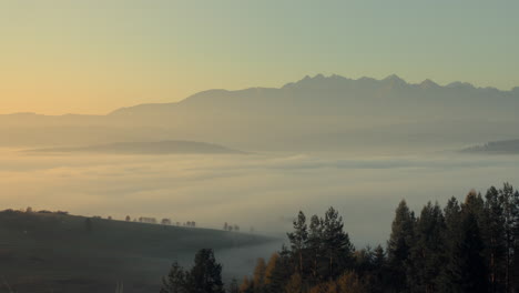 big rocky mountain peaks in the background with a mist covering the valley and small hills in the foreground captured at sunrise with golden sky