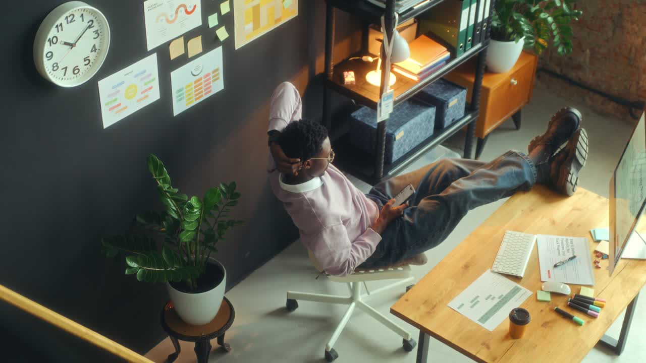 Relaxed Businessman Using Smartphone with Legs Resting on Desk in Office