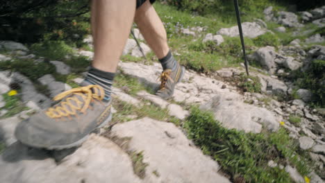 pierna de los excursionistas, caminando por un camino rocoso con bastones de senderismo en ropa de verano, parcialmente nublado con algunos rayos de sol