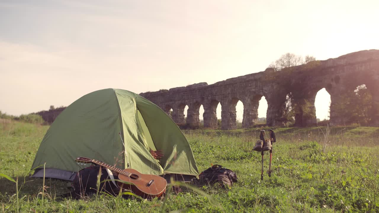 젊은 배여행자는 깨어나서 로마 수로 앞에 캠핑 텐트를 나가고, 파르코 데글리 아키도티 공원의 아치, 로마의 해가 지는 공원 유적, 지상에서 천천히 움직이는 지이.