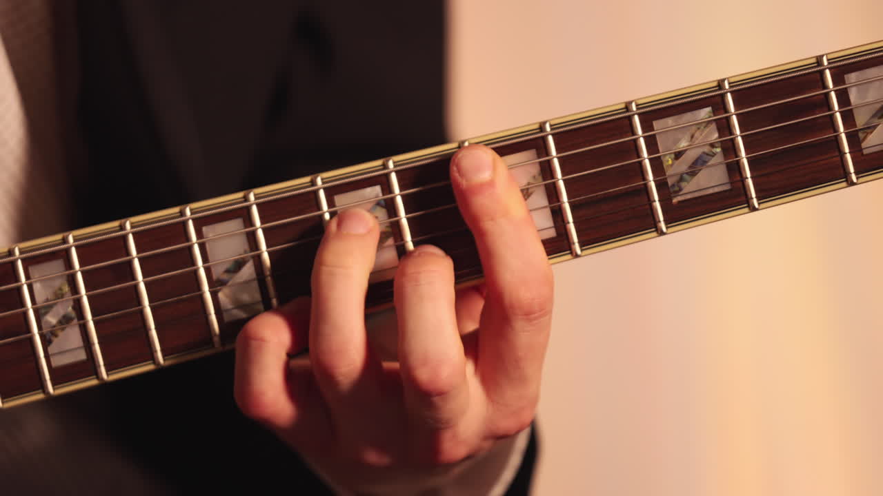 Primissimo piano della mano di un musicista che suona le corde della chitarra. La calda illuminazione interna mette in risalto i movimenti delle dita e i dettagli della tastiera.