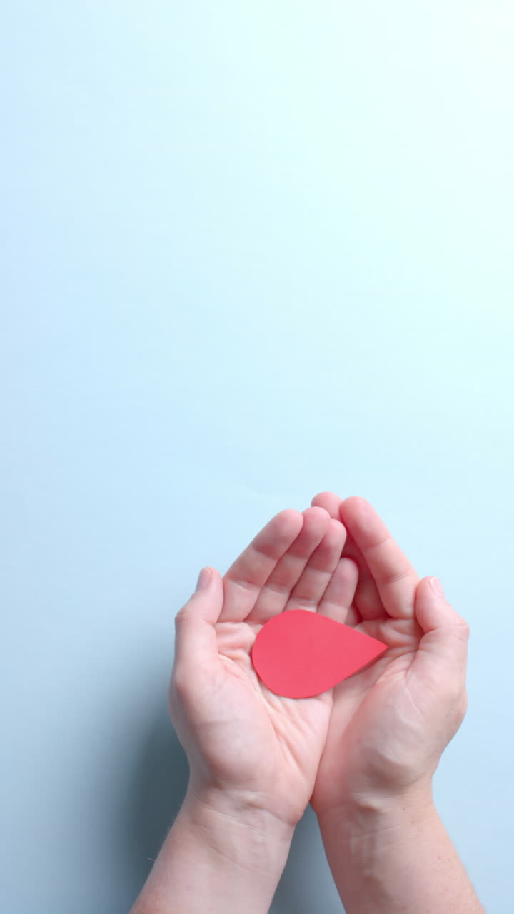 Vertical video of hands of caucasian man holding blood drop on blue background with copy space