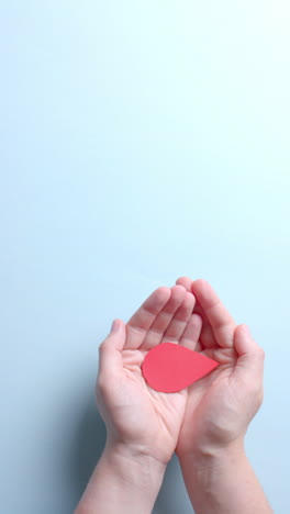 vertical video of hands of caucasian man holding blood drop on blue background with copy space