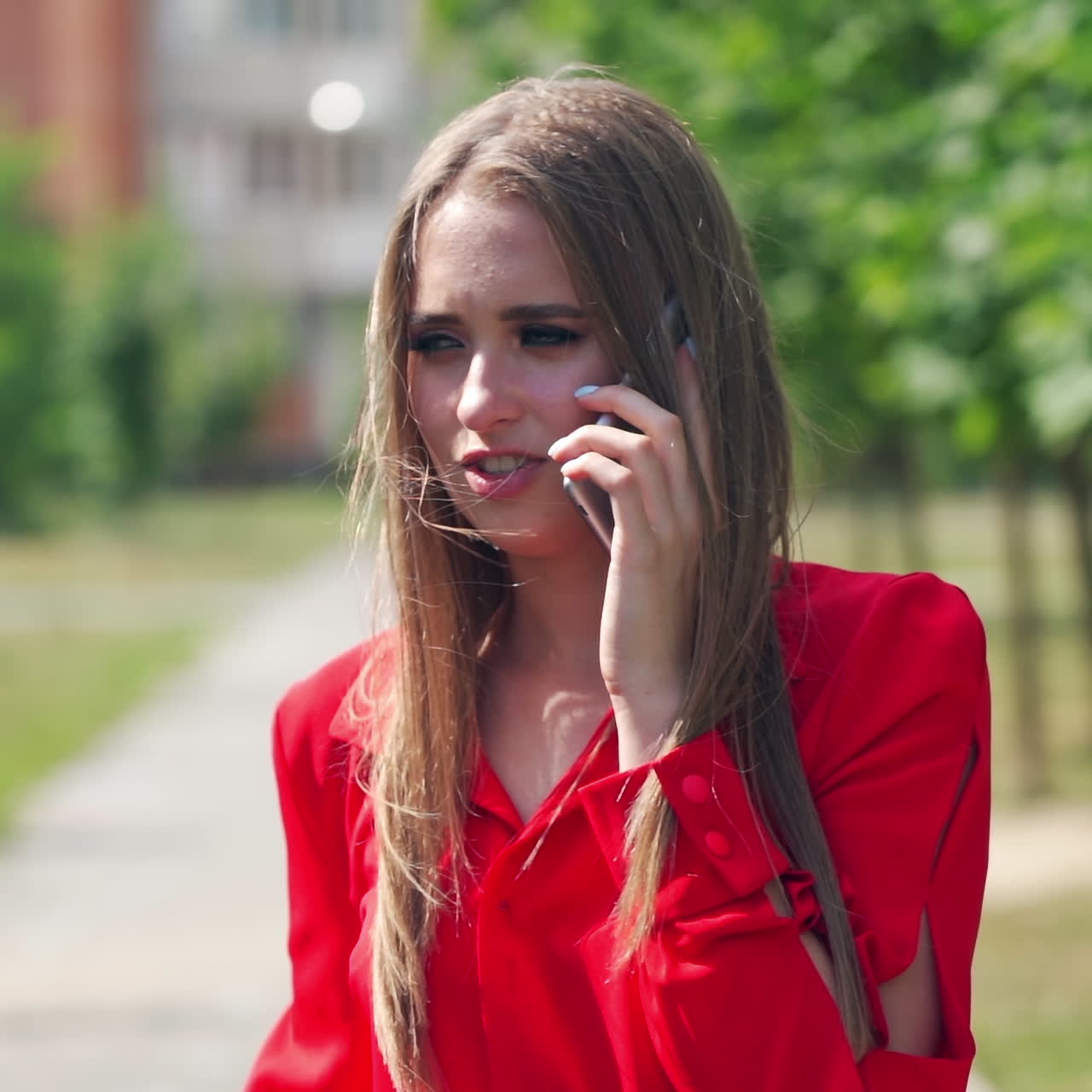Young woman talking on the phone. Portrait of a beautiful lady with long hair holding a mobile phone on the blurred city background. Slow motion.