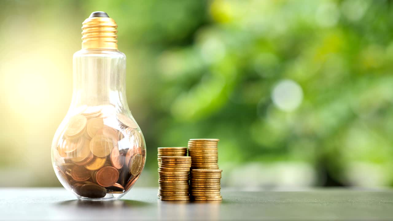 ahorro de energía. pilas de monedas en bombilla y árbol de movimiento fondo de la naturaleza. ahorro, contabilidad y concepto financiero. video 4k cámara lenta